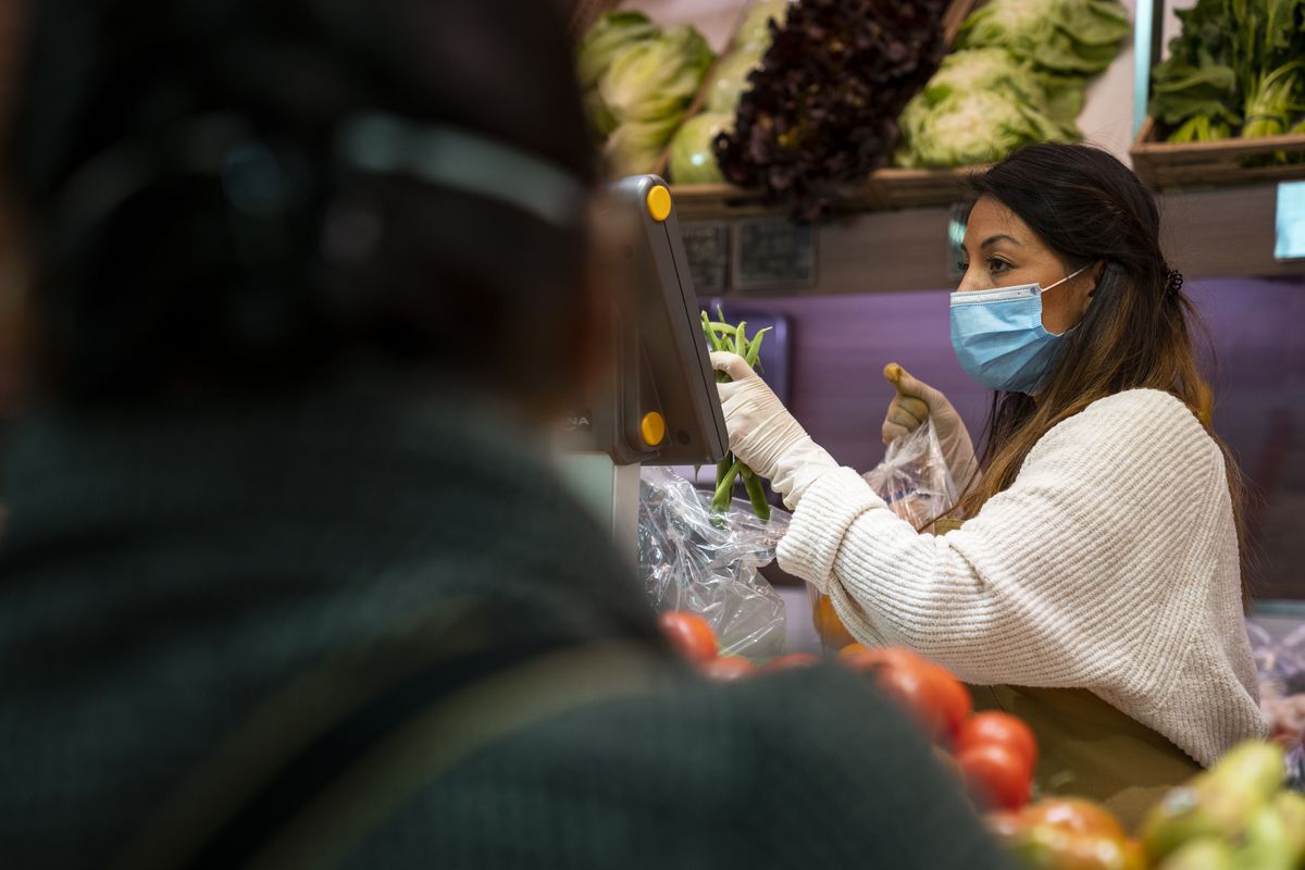 Una dependenta amb guants i mascareta atén els clients a la parada de fruites i verdures