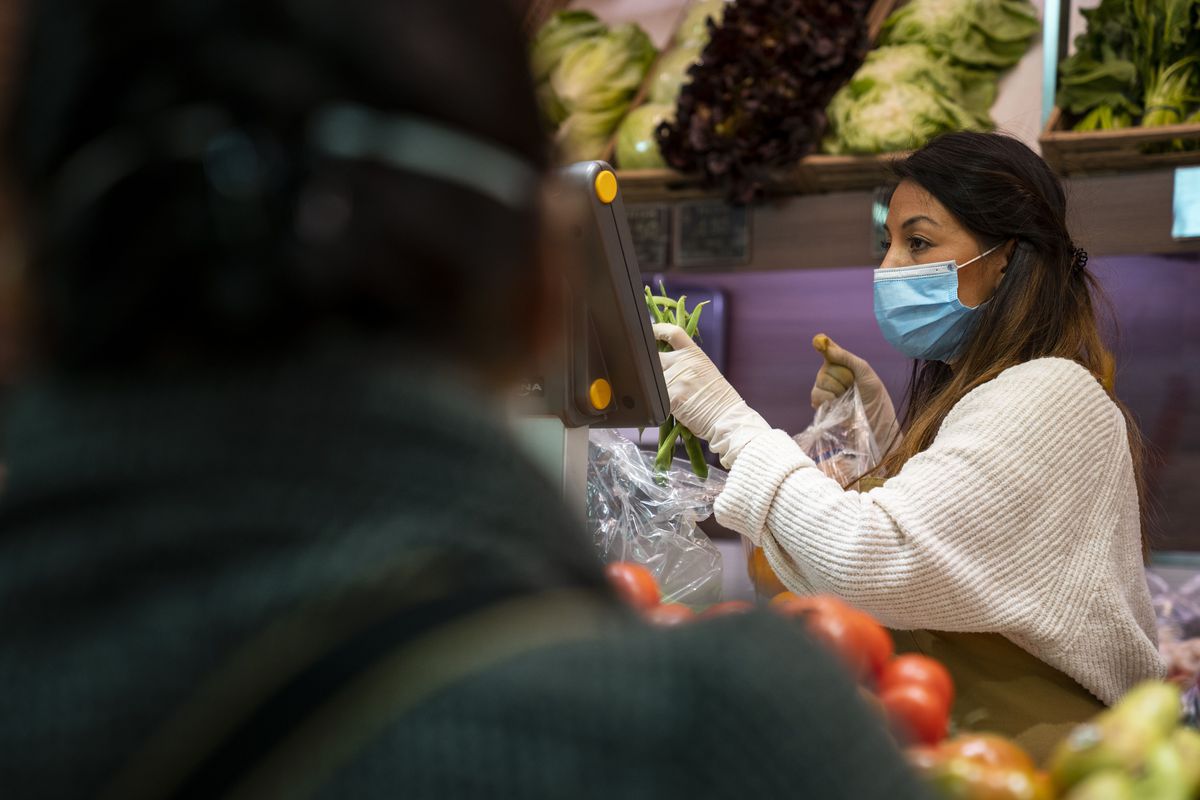 Una dependienta con guantes y mascarilla atiende a los clientes en el puesto de frutas y verduras